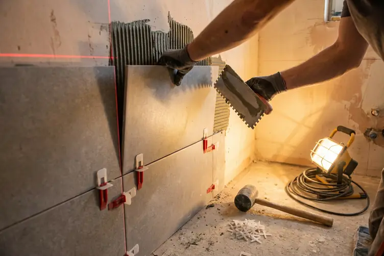 Carreleur posant du grès cérame grand format sur le mur d’une salle de bain en chantier